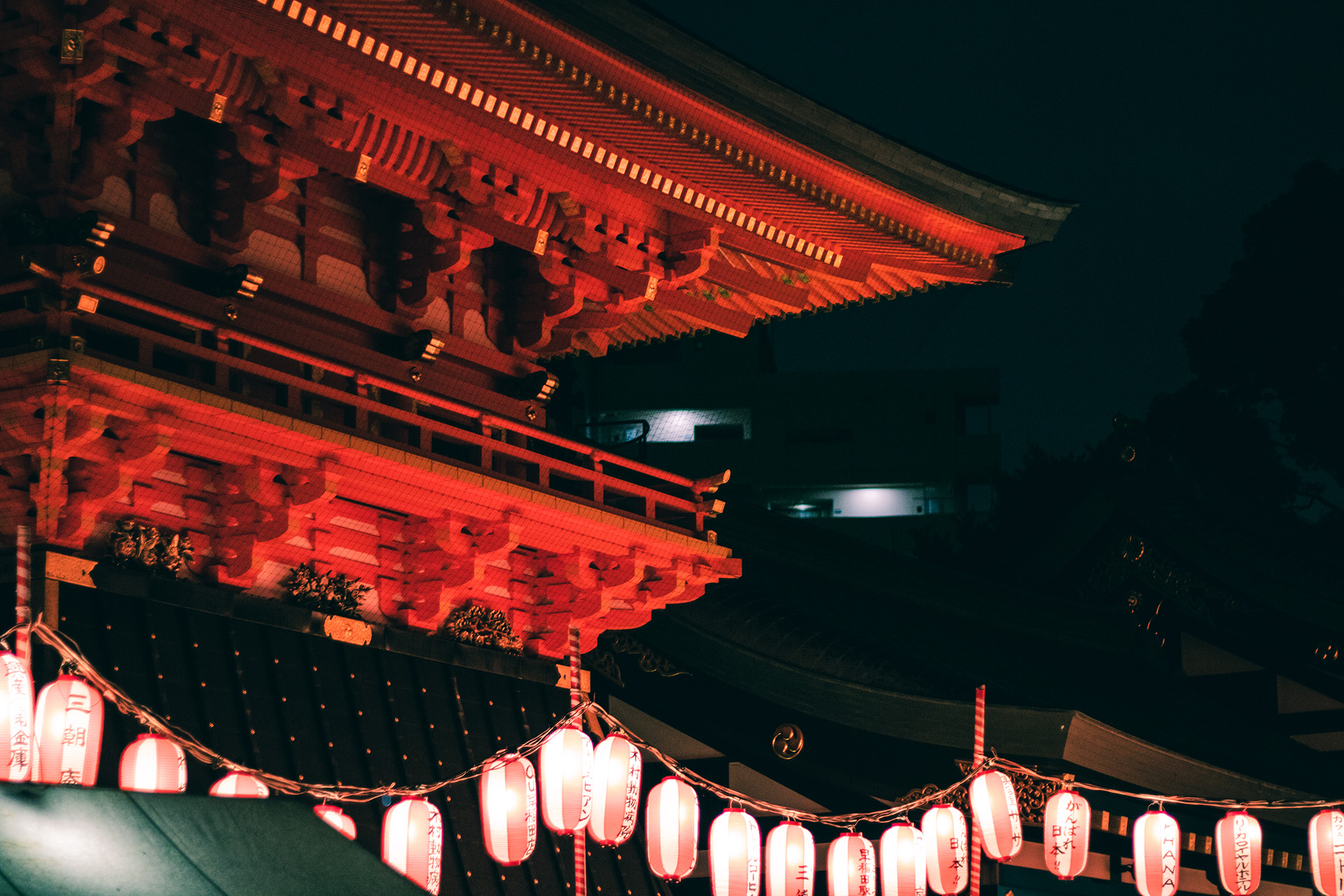 Close-up of a Japanese temple seen from the side at night with soft orange lighting from hanging lanterns.